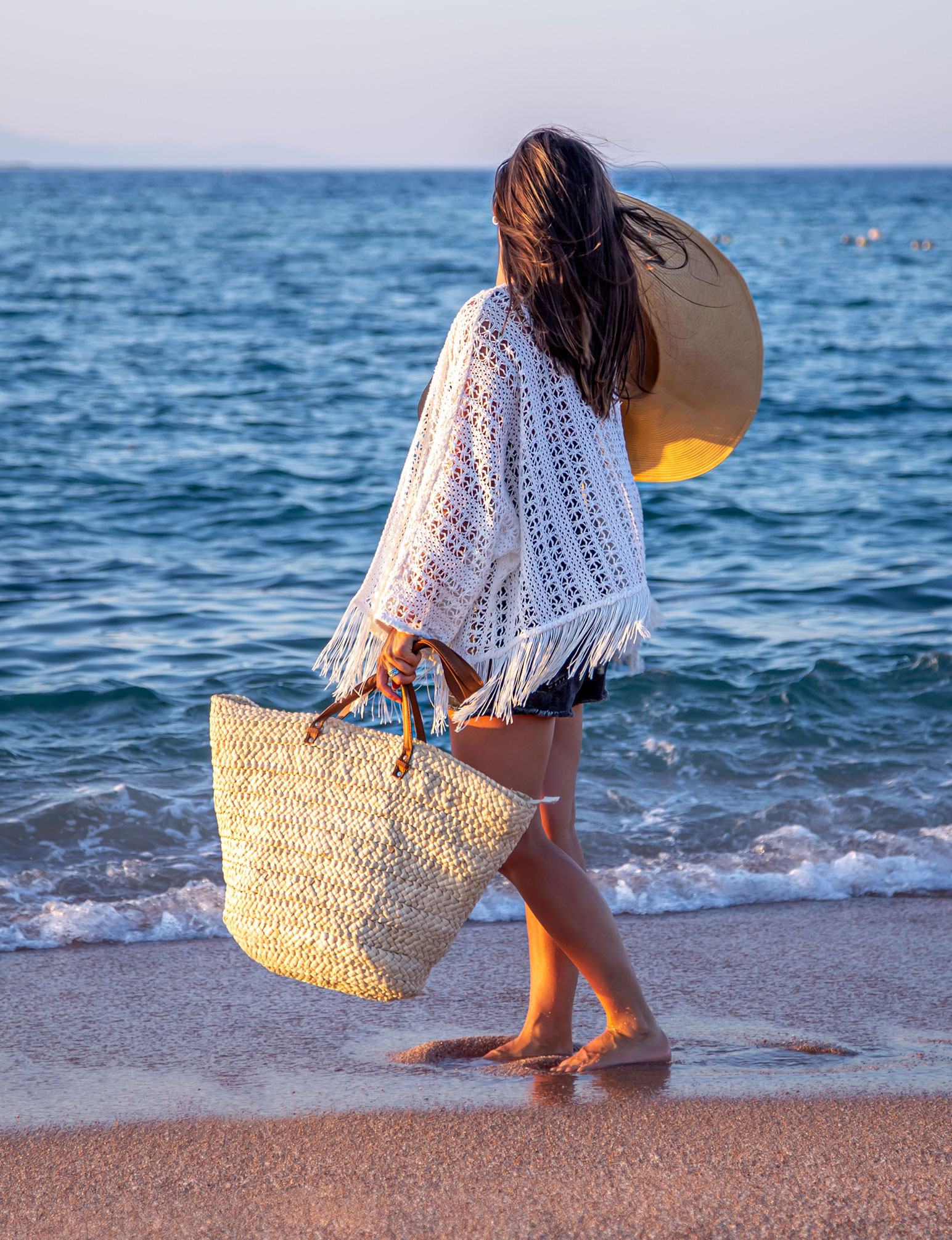 girl-with-hat-in-her-hands-and-wicker-bag-walks-on-the-seashore-summer-vacation-concept